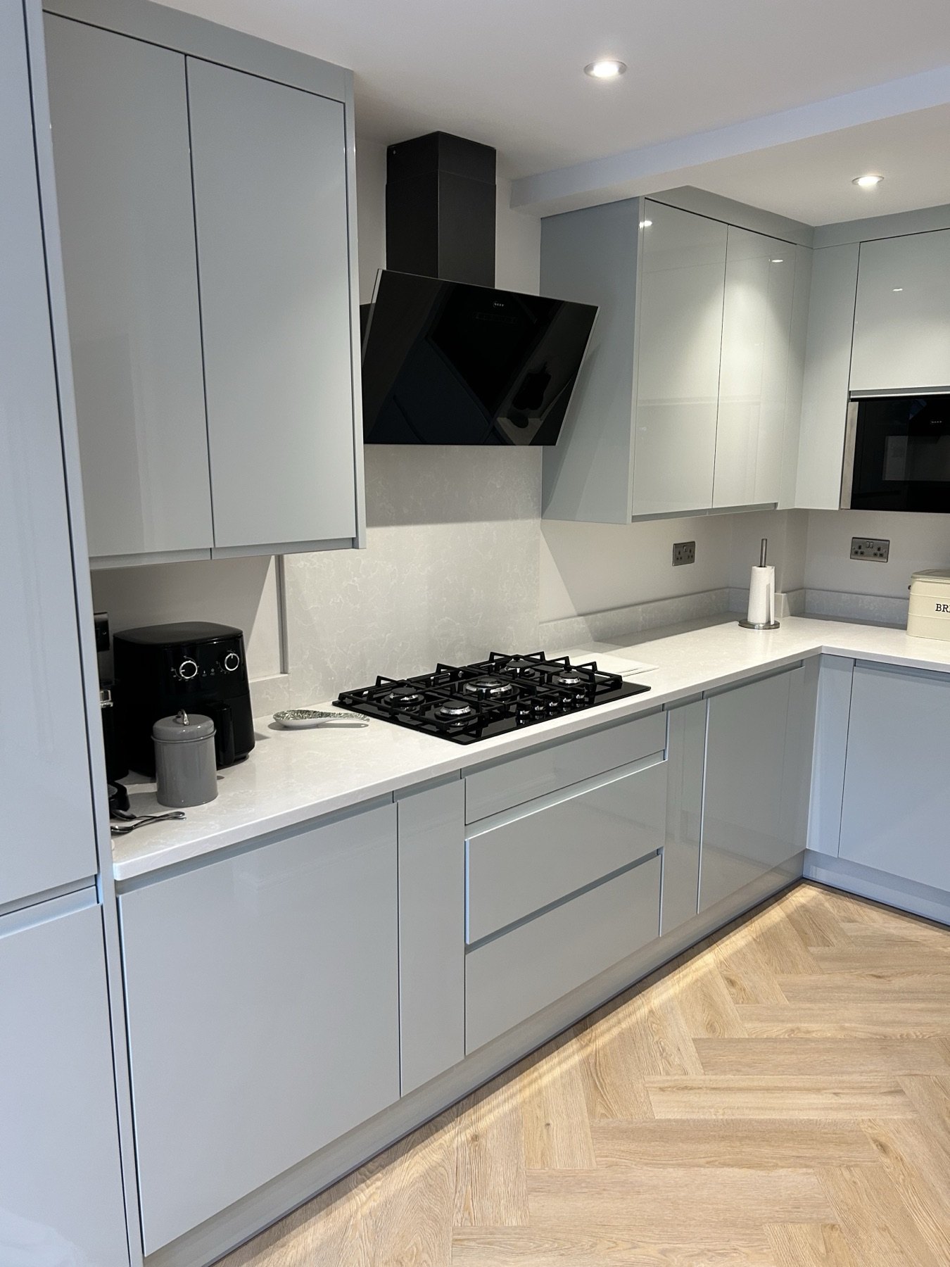Grey gloss handleless kitchen with gas hob and herringbone oak floor